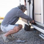 Man controleert de onderzijde van een caravan met gereedschap