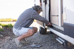Man controleert de onderzijde van een caravan met gereedschap