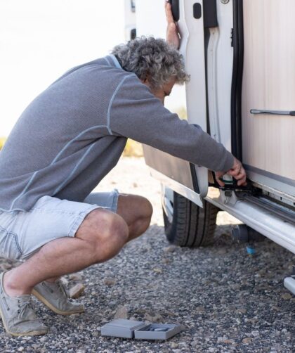 Man controleert de onderzijde van een caravan met gereedschap