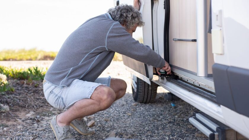 Man controleert de onderzijde van een caravan met gereedschap